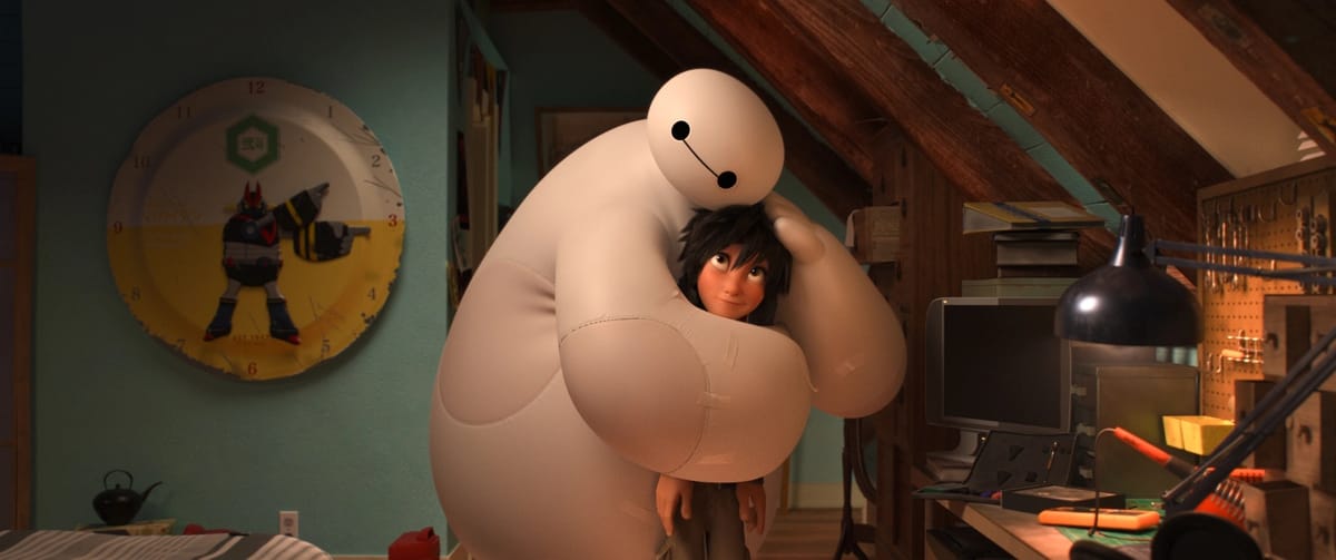 A very large humanoid robot, the white, vinyl Baymax, hugs the teenaged boy Hiro in his attic workshop.